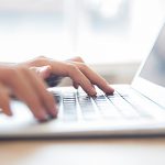 Close-up of male hands typing on laptop keyboard