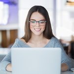 Portrait of cheerful student using laptop in cafe