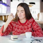 Young Woman Tasting Cake and Sitting at Cafe Table